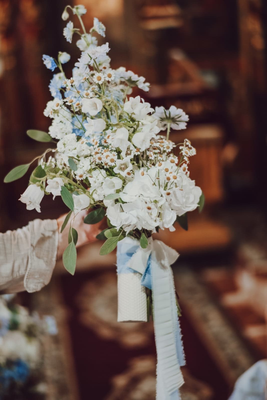 Buchet alb cu trandafiri și mușețel, ținut în mână la o ceremonie de botez